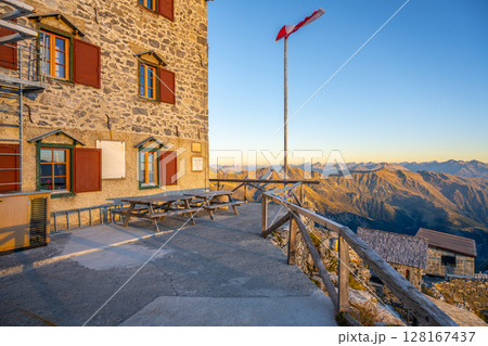 At sunrise, the Julius Payer House offers breathtaking views of the Ortler Alps. The building is surrounded by mountains and features benches for visitors to enjoy the landscape and fresh air. At sunrise, the Julius Payer House offers breathtaking views of the Ortler Alps. The building is surrounded by mountains and features benches for visitors to enjoy the landscape and fresh air. 128167437