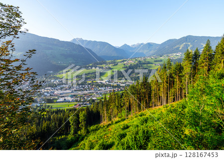 Early morning light illuminates the picturesque landscape of Schladming in Low Tauern, Austria, showcasing lush green hills and valleys under a clear blue sky. 128167453