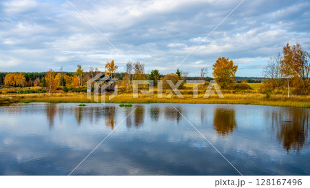 The tranquil Pernink peat bog in the Ore Mountains showcases vibrant autumn colors. Trees line the water's edge, reflecting beautifully in the calm surface under a partly cloudy sky. The tranquil Pernink peat bog in the Ore Mountains showcases vibrant autumn colors. Trees line the water's edge, reflecting beautifully in the calm surface under a partly cloudy sky. 128167496