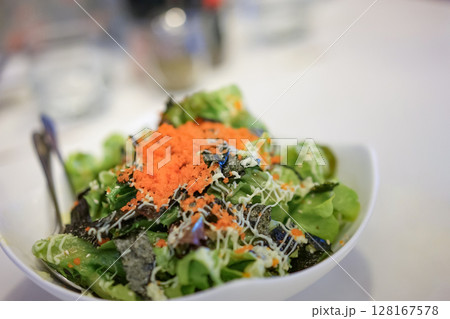 Green vegan salad from green leaves mix and vegetables, top view on white table. Green salad, close up by green vegetable, seaweed, and tobiko dressing on a white plate, isolated on white background. 128167578