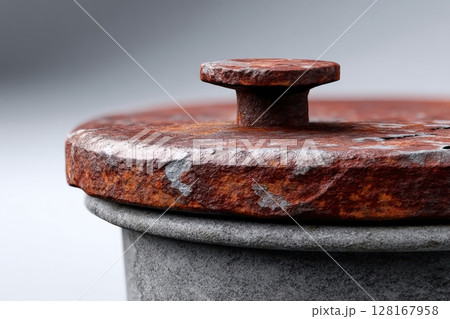 Rusty metal lid resting on a textured gray container in soft lighting 128167958