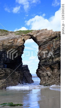 A stunning natural arch carved into towering sea cliffs on a sandy beach, with the ocean visible through the opening. A stunning natural arch carved into towering sea cliffs on a sandy beach, with the ocean visible through the opening. 128168101