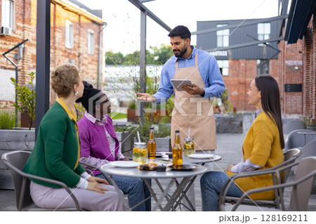 A waiter takes an order from customers at an outdoor restaurant. A waiter takes an order from customers at an outdoor restaurant. 128169211
