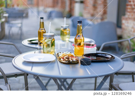 An outdoor restaurant table set with drinks, food, and plates, ready for dining. No people are present. 128169246