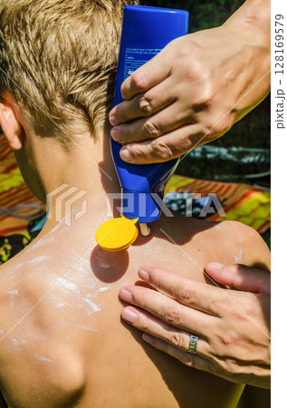 Parent applying sunscreen lotion from bottle on childs back for sun safety. High quality photo 128169579