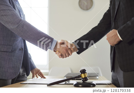 Male lawyer shaking hand with a man client standing at the desk on workplace in office. Male lawyer shaking hand with a man client standing at the desk on workplace in office. 128170338