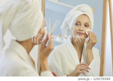 Woman applying skincare products to her face in bathroom Woman applying skincare products to her face in bathroom 128170389