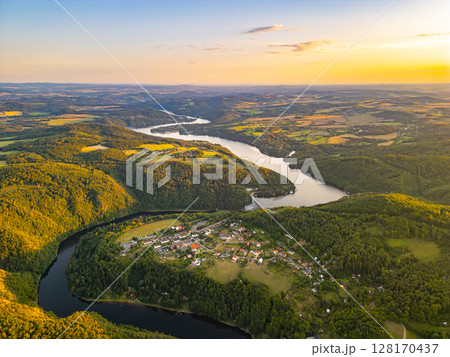 A breathtaking sunset illuminates the Slapy Water Reservoir, showcasing the serene landscape and vibrant colors. The tranquil waters reflect the hues of dusk, enhancing the natural beauty of the area. A breathtaking sunset illuminates the Slapy Water Reservoir, showcasing the serene landscape and vibrant colors. The tranquil waters reflect the hues of dusk, enhancing the natural beauty of the area. 128170437