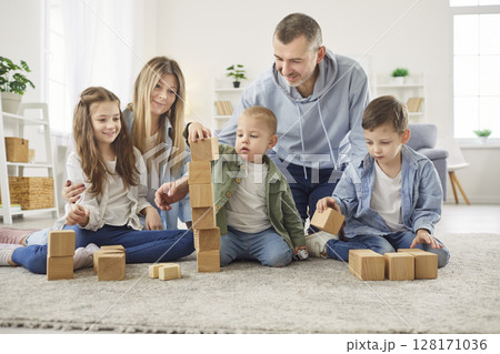 Happy family sitting on carpet, building wooden block tower and enjoying teamwork together at home. 128171036