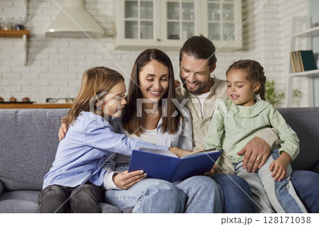 Happy parents and children sitting on the couch and reading a story book together Happy parents and children sitting on the couch and reading a story book together 128171038