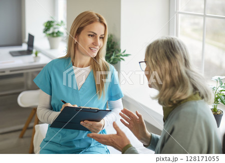 Friendly smiling nurse listening to senior woman during medical consultation near bright window. Friendly smiling nurse listening to senior woman during medical consultation near bright window. 128171055