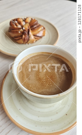 Cup of hot coffee served with a traditional Swedish cinnamon bun on a rustic plate. This image represents a cozy fika moment and Scandinavian coffee culture concept 128171128