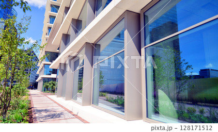 City life, urban landscape and ecology. Modern office complex with glass facades and smooth lines against backdrop of green trees, concept of modern architecture. Organically building into nature. City life, urban landscape and ecology. Modern office complex with glass facades and smooth lines against backdrop of green trees, concept of modern architecture. Organically building into nature. 128171512