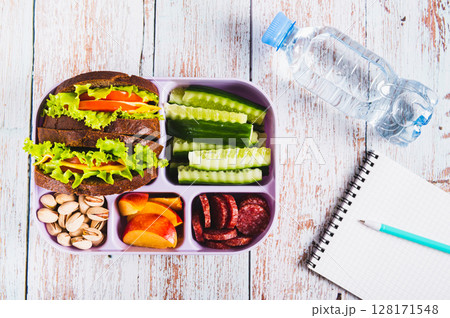 Lunch box with food, bottle of water, notebook and pen on the table top view Lunch box with food, bottle of water, notebook and pen on the table top view 128171548