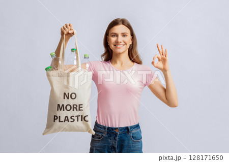 Portrait Of Positive Young Lady Holding Eco Bag With No More Plastic Inscription And Empty Bottles Inside, Showing Ok Gesture, Cheerful Millennial Woman Posing On Light Studio Background, Free Space Portrait Of Positive Young Lady Holding Eco Bag With No More Plastic Inscription And Empty Bottles Inside, Showing Ok Gesture, Cheerful Millennial Woman Posing On Light Studio Background, Free Space 128171650