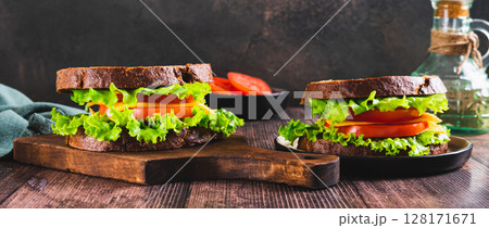 Vegetarian sandwich with tomato, cheese and lettuce on a board on a table web banner Vegetarian sandwich with tomato, cheese and lettuce on a board on a table web banner 128171671