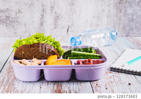 Lunch box with food, bottle of water, notebook and pen on the table 128171681