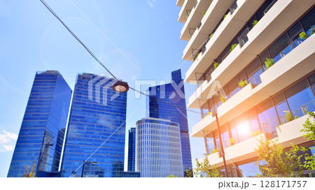 City life, urban landscape and ecology.  Modern office complex with glass facades and smooth lines against backdrop of green trees, concept of modern architecture. Organically building into nature.   128171757