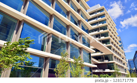 City life, urban landscape and ecology. Modern office complex with glass facades and smooth lines against backdrop of green trees, concept of modern architecture. Organically building into nature. City life, urban landscape and ecology. Modern office complex with glass facades and smooth lines against backdrop of green trees, concept of modern architecture. Organically building into nature. 128171779