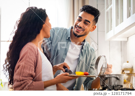Happy Middle Eastern Spouses Preparing Lunch Together In Kitchen, Cheerful Young Arab Lovers Enjoying Cooking Healthy Food At Home, Making Delicious Vegetable Meal On A Stove, Closeup Shot 128171794