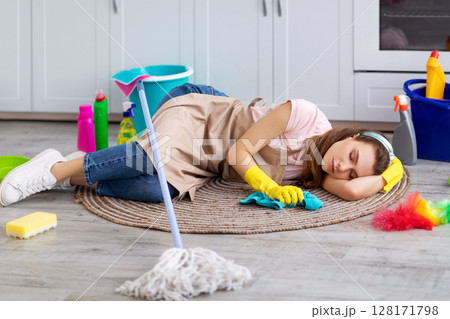 Tired young woman sleeping on floor at kitchen, surrounded by cleaning supplies, exhausted from housework, taking break from domestic duties. Overworked lady napping while doing house chores Tired young woman sleeping on floor at kitchen, surrounded by cleaning supplies, exhausted from housework, taking break from domestic duties. Overworked lady napping while doing house chores 128171798