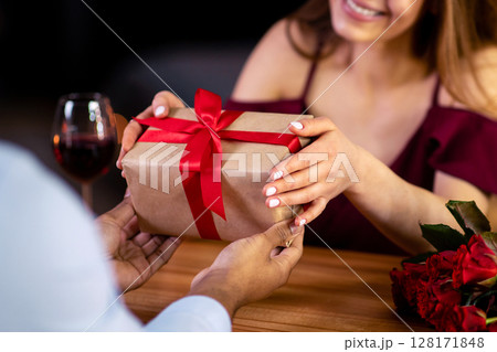 Loving woman surprising her black boyfriend with romantic present for valentine's day during romantic dinner in restaurant, giving wrapped gift box, interracial couple celebrating anniversary, cropped Loving woman surprising her black boyfriend with romantic present for valentine's day during romantic dinner in restaurant, giving wrapped gift box, interracial couple celebrating anniversary, cropped 128171848