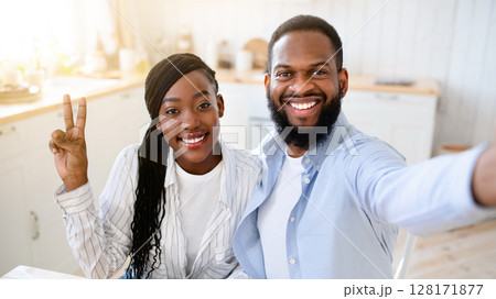 Cheerful Black Spouses Taking Selfie While Drinking Morning Coffee Together, Happy African American Couple Posing For Photo, Sitting At Table In Kitchen And Smiling At Camera, Closeup Shot 128171877