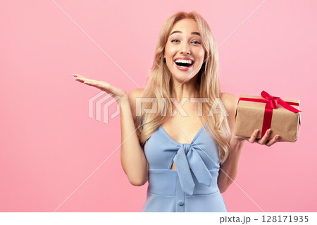Gifts and presents. Happy Caucasian lady holding wrapped box, feeling excited on pink studio background. Lovely blonde model receiving holiday surprise, celebrating Woman's Day Gifts and presents. Happy Caucasian lady holding wrapped box, feeling excited on pink studio background. Lovely blonde model receiving holiday surprise, celebrating Woman's Day 128171935