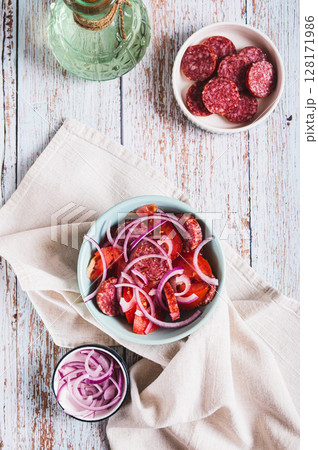 Chorizo sausage salad, tomatoes and onions on a plate on the table top and vertical view 128171986