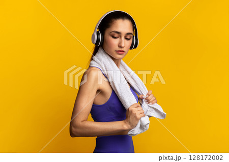 Music For Motivation. Portrait Of Determined Young Sportive Lady Wearing Wireless Headset Listening To Playlist Standing Isolated Over Orange Studio Background With White Towel Aroung Neck 128172002