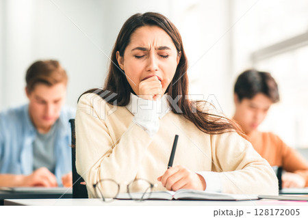Portrait of tired female student yawning sitting at desk in classroom. Female exhausted from getting ready for test or writing coursework, feeling sleepy during lecture in highschool. Lack of sleep Portrait of tired female student yawning sitting at desk in classroom. Female exhausted from getting ready for test or writing coursework, feeling sleepy during lecture in highschool. Lack of sleep 128172005