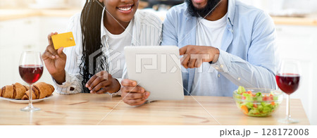Ordering Food Online. Happy Black Couple With Digital Tablet And Credit Card In Kitchen Purchasing Meal Delivery Or Shopping Groceries From Internet, Sitting At Table Together, Copy Space 128172008
