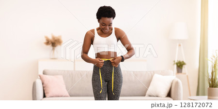 Joyful Black Female Measuring Waist Standing On Scales Excited About Successful Weight Loss Result At Home. Slim Woman Making Measurement During Diet. Slimming And Weight-Loss. Full Length Joyful Black Female Measuring Waist Standing On Scales Excited About Successful Weight Loss Result At Home. Slim Woman Making Measurement During Diet. Slimming And Weight-Loss. Full Length 128172072