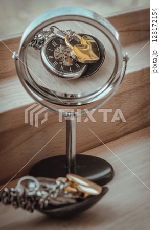 Golden heart shaped love padlock lap over A retro pocket watch with reflection in a circular mirror on wooden desk. 128172154