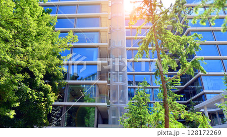Sustainable glass office building with trees for reducing carbon dioxide. Eco-friendly building in modern city. Office with green environment. Corporate building reduce CO2. Sustainable glass office building with trees for reducing carbon dioxide. Eco-friendly building in modern city. Office with green environment. Corporate building reduce CO2. 128172269