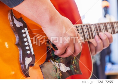 Musician strumming bright orange acoustic guitar, showing hand technique and fret detail Musician strumming bright orange acoustic guitar, showing hand technique and fret detail 128172551