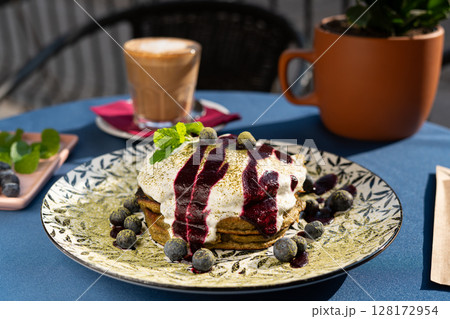 Fluffy matcha pancakes topped with juicy blueberries and velvety whipped cream, adorned with fresh mint leaves. Served on a white plate, glowing in morning sunlight a vibrant, delicious breakfast Fluffy matcha pancakes topped with juicy blueberries and velvety whipped cream, adorned with fresh mint leaves. Served on a white plate, glowing in morning sunlight a vibrant, delicious breakfast 128172954