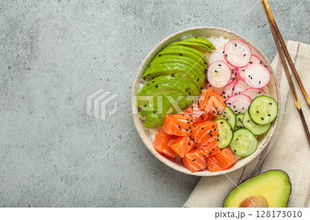 Salmon poke bowl with avocado, radish, cucumber and rice on grey background top view, space for text 128173010