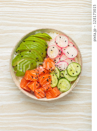Salmon poke bowl with avocado, radish, cucumber and rice on white wooden background top view 128173015