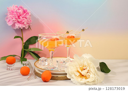 Ice punch with apricots, Modern still life with summer alcoholic cocktail and peonies on modern sunny background. Minimal summer party concept, advertising banner for bar, cafe Ice punch with apricots, Modern still life with summer alcoholic cocktail and peonies on modern sunny background. Minimal summer party concept, advertising banner for bar, cafe 128173019