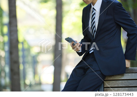 ビジネス街でスマートフォンを見るスーツの若いビジネスマン 128173443