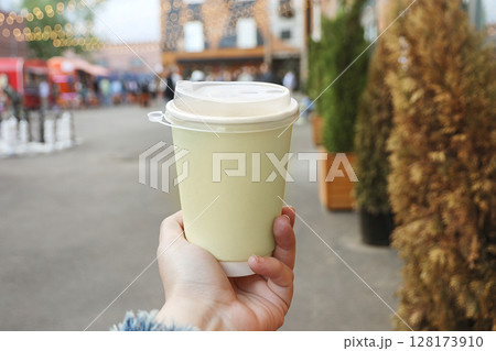 paper creamy color cup of drink in women's hand on evening street paper creamy color cup of drink in women's hand on evening street 128173910