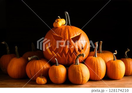 Carved jack-o-lantern surrounded by mini orange pumpkins 128174210