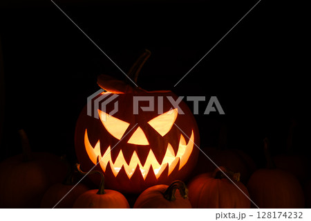 Illuminated jack-o'-lantern glows warmly in the center of small pumpkins 128174232
