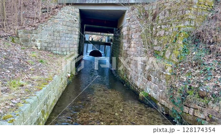 A Serene Waterway that Flows Gracefully Underneath a Beautiful, Grand Stone Archway 128174354