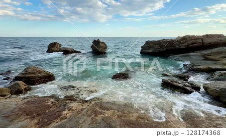 A Serene Coastal View Featuring Turquoise Waves Crashing Against Rugged Rocks Nearby A Serene Coastal View Featuring Turquoise Waves Crashing Against Rugged Rocks Nearby 128174368
