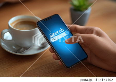 Closeup of male hands interacting with smartphone screen while holding coffee cup on a wooden table 128175102