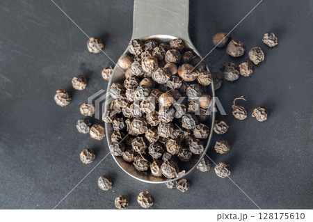 Raw organic black peppercorns or Dry black pepper seeds in stainless steel spoon on dark background. Raw organic black peppercorns or Dry black pepper seeds in stainless steel spoon on dark background. 128175610