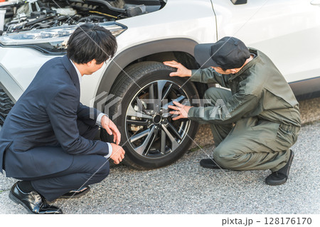 車の前で会話するスーツ姿のビジネスマンとつなぎ姿の自動車整備士の男性メカニック 128176170