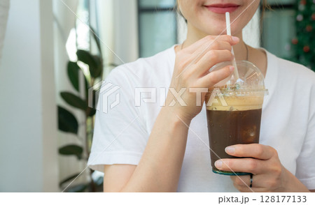 Cropped shot view of woman drinking an iced Americano coffee. An iced americano is a refreshing coffee drink made with espresso and cold water, served over ice. 128177133